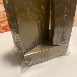 May include: Four olive-green rectangular blocks, wrapped in clear plastic. The blocks are stacked, with two forming a base and two resting on top. The packaging is slightly wrinkled, and the blocks have a slightly rough texture.