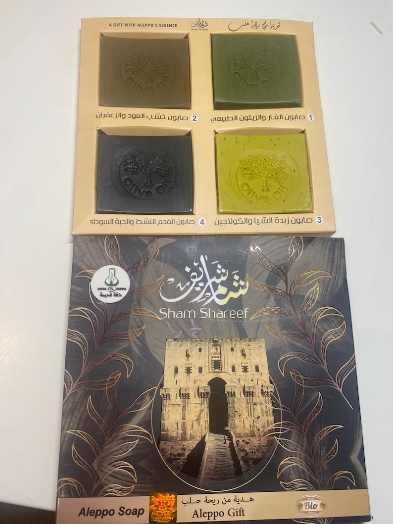 May include: A gift set of four olive oil soaps in a cardboard box. The soaps are labeled with Arabic text and the words "Olive Oil". The box is decorated with a picture of a building and the words "Sham Shareef" and "Aleppo Gift".