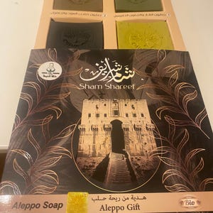 May include: A gift box set of four bars of Aleppo soap. The box is brown with a gold design and the text "Sham Shareef" and "Aleppo Gift". The soap bars are green and brown.