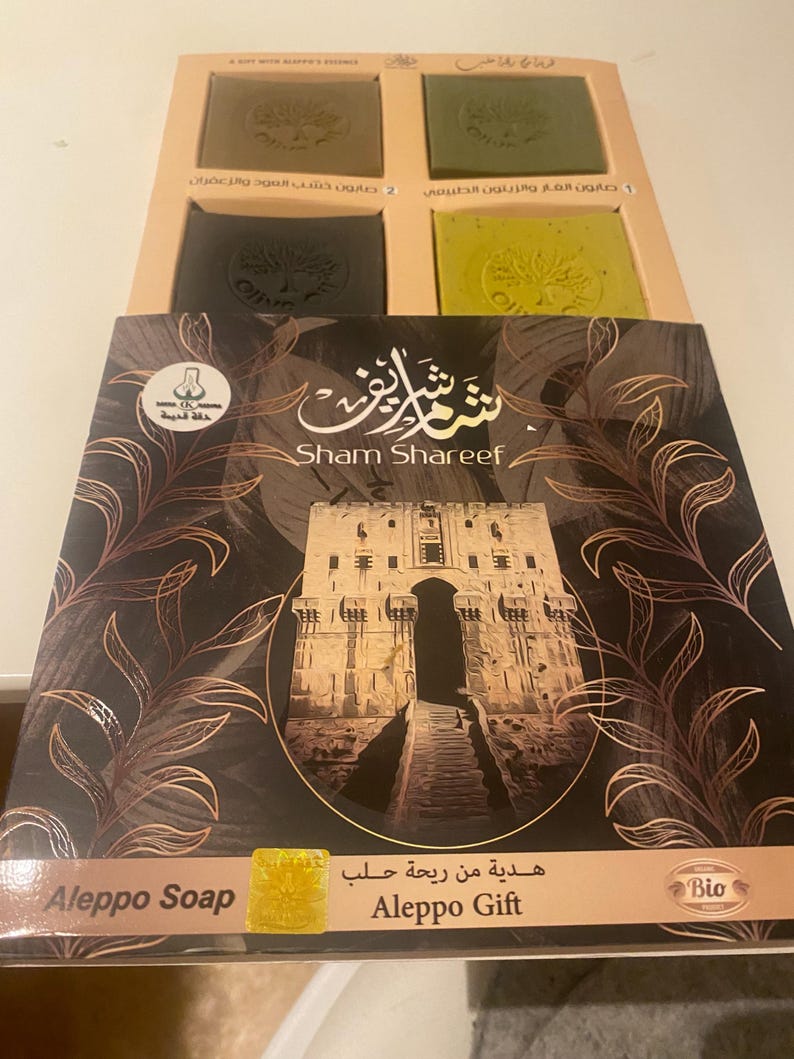 May include: A gift box set of four bars of Aleppo soap. The box is brown with a gold design and the text "Sham Shareef" and "Aleppo Gift". The soap bars are green and brown.