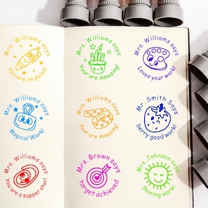 Pode incluir: Uma coleção de carimbos auto-entintados coloridos com vários desenhos e frases, incluindo "Você é incrível!" e "Trabalho mágico!". Os carimbos têm tampas vermelhas, amarelas, laranjas, rosas, roxas, azuis e verdes. Para professores.