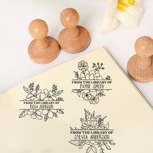 May include: Wooden stamps with floral designs and the text "FROM THE LIBRARY OF" followed by names. The stamps have a round base and a rounded handle. The names include Rosa Johnson, Payne Smith, and Sylvia Anderson.