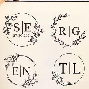 May include: A wooden handle rubber stamp positioned above a page displaying four black ink impressions of circular floral monograms. The designs feature the letters S|E with the date 27.30.2024, R|G, E|N, and T|L, all framed by delicate botanical leaf and flower illustrations.