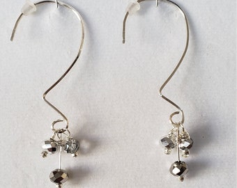 May include: A pair of silver hoop earrings with a dangling charm of three silver beads. The beads are faceted and have a clear, iridescent finish.