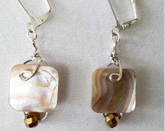 May include: A pair of silver earrings with a square-shaped iridescent shell pendant and a gold-toned bead hanging from each. The earrings have a leverback closure.
