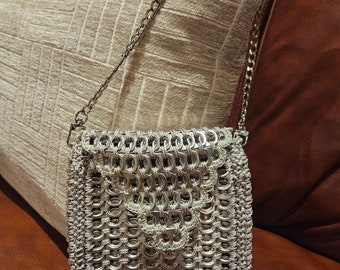 May include: A silver crocheted bag with a chain strap. The bag is made from recycled aluminum can tabs.