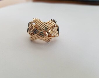 May include: A gold ring with a woven design. The ring is made of multiple strands of gold wire that are intertwined to create a complex pattern.