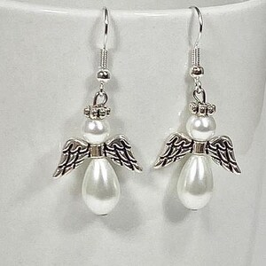 May include: A pair of silver angel earrings with white pearl accents. The angels have wings and a halo.