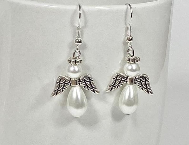 May include: A pair of silver angel earrings with white pearl accents. The angels have wings and a halo.