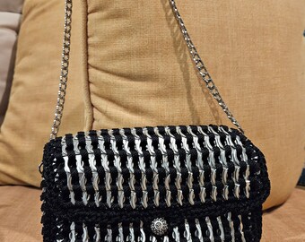 May include: A black and silver purse made from woven aluminum can tabs with a silver chain strap.