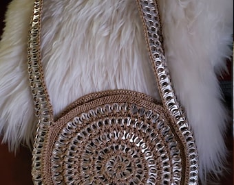 May include: A round, crocheted bag made from pull tabs. The bag has a long strap and is a light brown color.