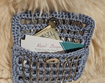 May include: A handmade blue wallet crafted from recycled aluminum can tabs and blue yarn. The wallet is open, revealing a twenty-dollar bill, business cards, and a coin. The text "Regali - Designs Gifts from the Heart" is visible on a card.