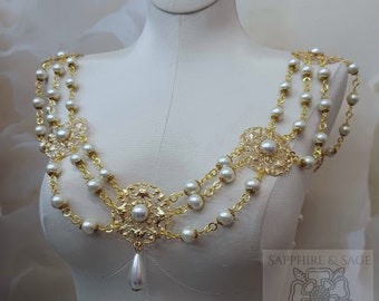 May include: A gold and white pearl necklace with a delicate floral design. The necklace is made of multiple strands of pearls and gold chain, with a large floral pendant in the center. The necklace is displayed on a white mannequin.