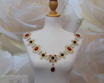 May include: A gold necklace with red and black gemstones, white pearls, and a dangling red gemstone pendant. The necklace is on a white mannequin against a white floral background.