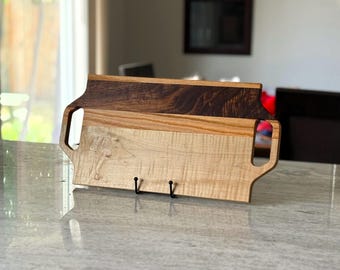 May include: A rectangular wooden serving tray featuring two integrated side handles. The tray is constructed from three distinct horizontal wood panels, showcasing a dark brown top section, a medium brown middle strip, and a light tan bottom section.