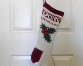 Könnte beinhalten: Ein weißer, gestrickter Weihnachtssocken mit roter Manschette und einem grünen Stechpalmen-Design. Der Socken trägt den Namen "KENNEDY" auf der Vorderseite.