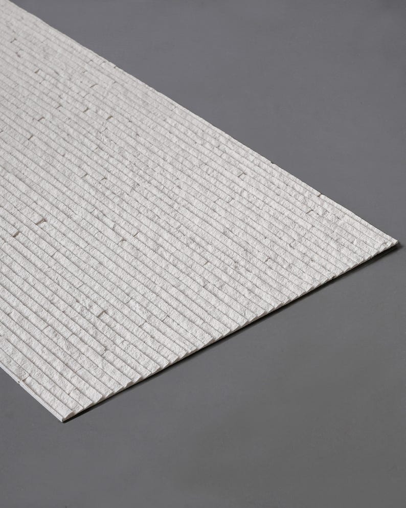 K&ouml;nnte beinhalten: Ein rechteckiges Wandpaneel mit einem Stapelstein-Design in einer strukturierten, cremewei&szlig;en Ausf&uuml;hrung. Die Oberfl&auml;che besteht aus zahlreichen d&uuml;nnen, horizontalen Steinleisten, die in einem linearen Muster angeordnet sind und eine geschichtete Optik erzeugen.