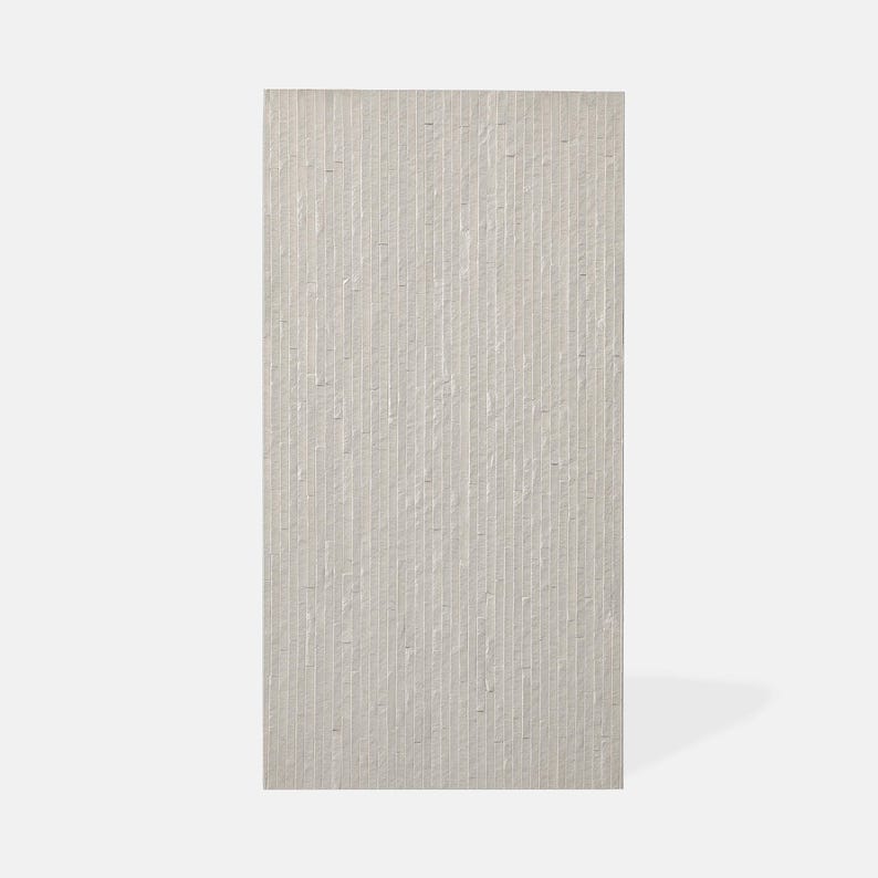 K&ouml;nnte beinhalten: Eine rechteckige Wandfliese in einem hellen Off-White- oder Cremeton. Die Oberfl&auml;che weist eine Reihe vertikaler, paralleler Rillen oder Rippen auf, die eine lineare Textur &uuml;ber die gesamte Fliesenfl&auml;che erzeugen und ihr ein strukturiertes Aussehen verleihen.