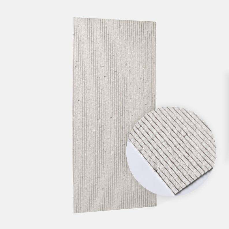 K&ouml;nnte beinhalten: Ein rechteckiges Wandpaneel mit vertikaler linearer Textur in einem hellen Off-White-Farbton. Die Oberfl&auml;che besteht aus schmalen, parallelen Streifen mit einer rauen, steinartigen Struktur. Ein kreisf&ouml;rmiger Ausschnitt zeigt eine vergr&ouml;&szlig;erte Ansicht.