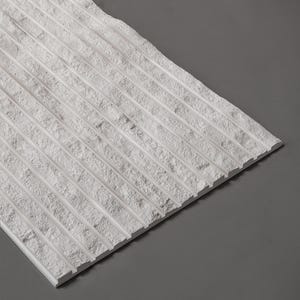 Può includere: Una piastrella rettangolare bianca con una superficie strutturata e scanalature parallele. La piastrella è angolata, rivelando i suoi bordi ruvidi e lo sfondo grigio. Il design suggerisce un'estetica moderna e minimalista, adatta all'interior design.