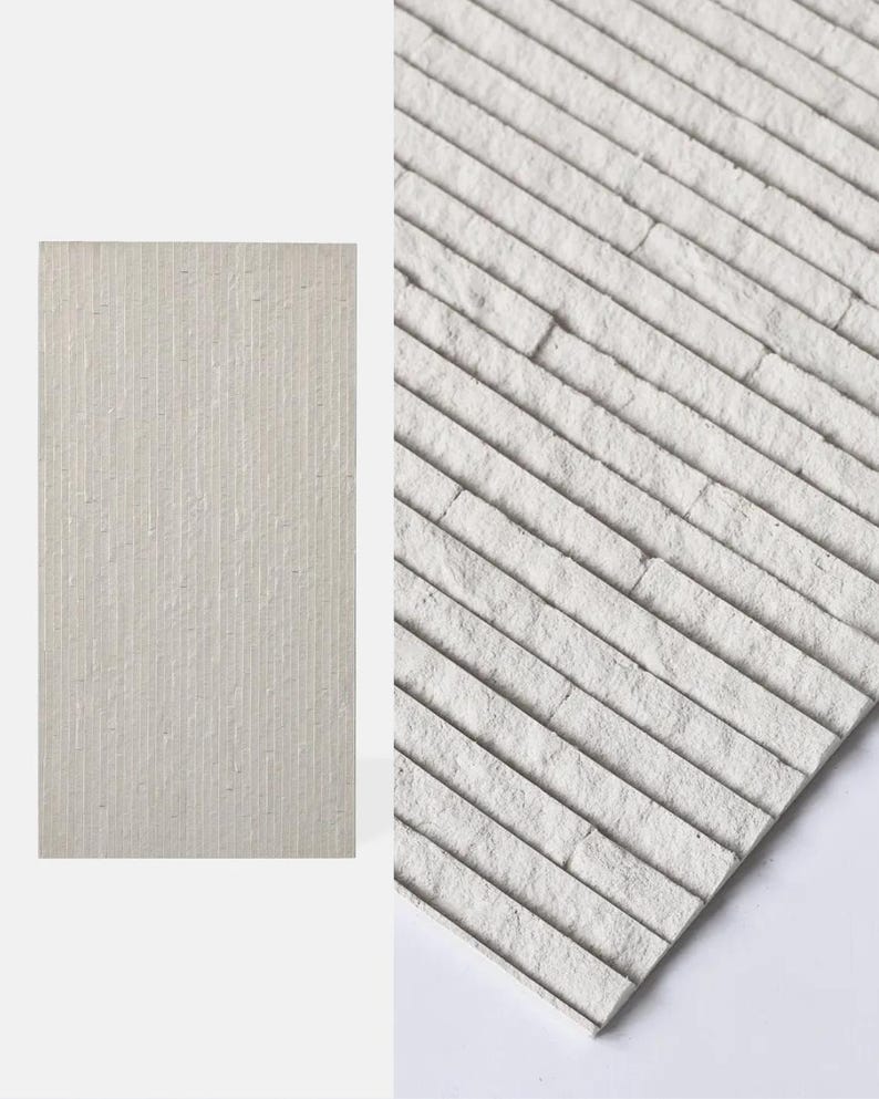 K&ouml;nnte beinhalten: Eine rechteckige Wandfliese in hellem Off-White mit einer strukturierten Oberfl&auml;che, die aus d&uuml;nnen, parallelen vertikalen Rippen besteht. Das Material hat ein mattes Finish mit einem leicht unebenen, natursteinartigen Erscheinungsbild.