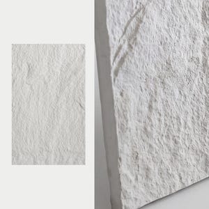 Könnte beinhalten: Eine rechteckige weiße Steinplatte mit einer rauen, unebenen und strukturierten Oberfläche. Das Material weist ein natürliches, zerklüftetes Aussehen mit tiefen Spalten und erhabenen Graten auf der gesamten Vorderseite sowie ein mattes Finish auf.