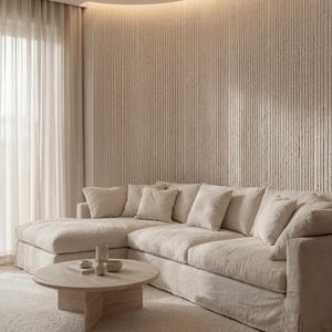 K&ouml;nnte beinhalten: Ein beiges Ecksofa mit mehreren passenden Zierkissen, kombiniert mit einem runden Couchtisch aus Holz mit kreuzf&ouml;rmigem Fu&szlig;. Die M&ouml;bel stehen vor einer strukturierten Wand mit vertikalen Rillen und integrierter indirekter Beleuchtung.