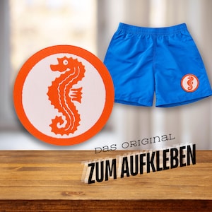 Könnte beinhalten: Runder Aufkleber in Orange und Weiß mit einem Seepferdchen-Motiv. Unter dem Aufkleber steht der Text "Das Original zum Aufkleben".