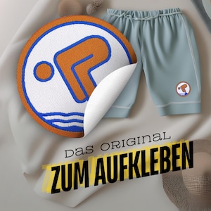 Könnte beinhalten: Ein weißer Stoffhintergrund mit einem blauen und orangefarbenen gestickten Patch eines Tauchers. Der Patch ist an einer hellblauen Badehose befestigt. Der Text "Das Original zum Aufkleben" ist in Schwarz auf gelbem Hintergrund gedruckt.