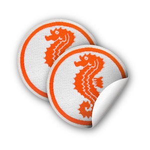 Könnte beinhalten: Zwei runde Stoffpatches in Weiß mit orangefarbenen gestickten Seepferdchen-Motiven. Die Patches haben eine abziehbare Klebefläche.