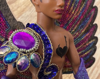 May include: A black doll with a purple and blue sequined costume and large wings. The doll has a black heart tattoo on its chest and is wearing a purple and blue sequined skirt.
