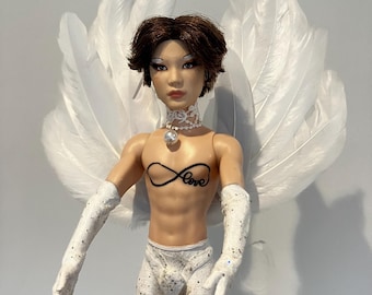 May include: A doll with brown hair and white wings wearing a white lace collar, white gloves, white underwear, and white fishnet stockings. The doll has a tattoo on its chest that says "Love" inside an infinity symbol.