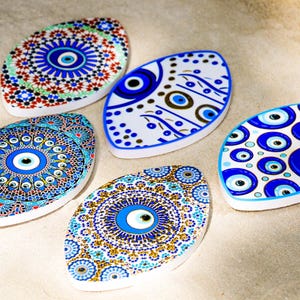 Può includere: Cinque amuleti in ceramica di occhio turco in vari motivi blu e bianchi. Ogni amuleto ha la forma di un ovale e presenta un occhio blu al centro.
