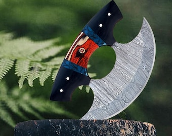May include: A curved, silver-colored knife with a black handle. The handle has a red, blue, and white pattern. The knife is resting on a wooden surface.