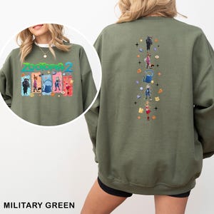 K&ouml;nnte beinhalten: Milit&auml;rgr&uuml;nes Sweatshirt mit dem Text "Zootopia 2" und Cartoon-Figuren auf der Vorderseite. Die R&uuml;ckseite hat ein vertikales Design mit weiteren Cartoon-Figuren. Das Sweatshirt ist aus einem weichen Material gefertigt.