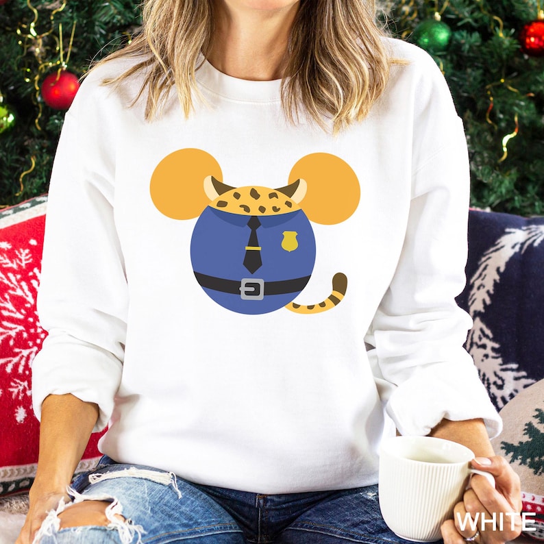 May include: White sweatshirt featuring a cartoon design of a leopard in a police uniform. The leopard's head is designed with Mickey Mouse ears. The leopard is wearing a blue uniform with a black tie and belt. The design includes a yellow badge and a striped tail.