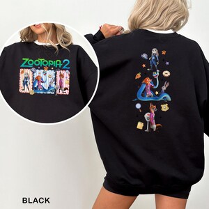 May include: Black sweatshirt featuring the text "ZOOTOPIA 2" in colorful lettering. The front graphic includes cartoon characters. The back of the sweatshirt has a larger graphic with more characters and themed objects. The sweatshirt is a crew neck style.