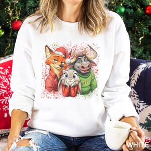 May include: White sweatshirt featuring a colorful graphic of three cartoon animals: a fox in a Santa hat, a bunny, and a bull. The graphic is decorated with red and green paint splatters, perfect for the holiday season.
