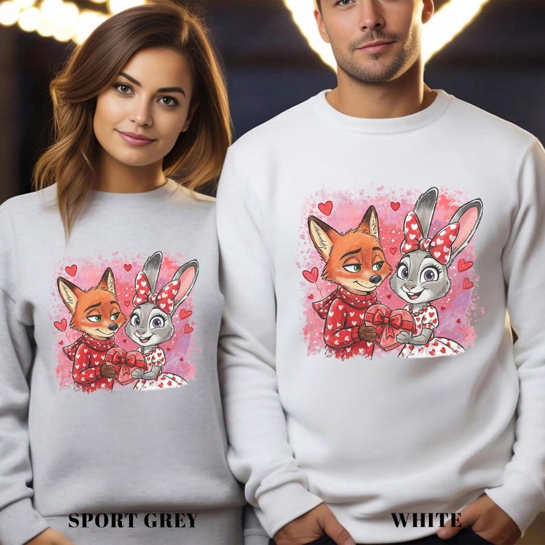 May include: Sport grey and white sweatshirts featuring a cartoon fox and bunny holding a heart-shaped gift. The fox wears a red scarf and the bunny wears a red bow. The sweatshirts have the words "SPORT GREY" and "WHITE" printed at the bottom.