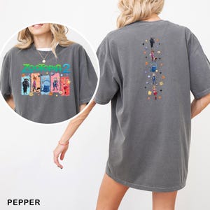 Op de afbeelding: Peppergrijze t-shirt met een kleurrijke "Zootopia 2" afbeelding op de voor- en achterkant. De afbeelding op de voorkant toont de filmtitel en personages. De afbeelding op de achterkant toont een verticale rangschikking van personages en iconen. Het shirt heeft een losse, oversized pasvorm.