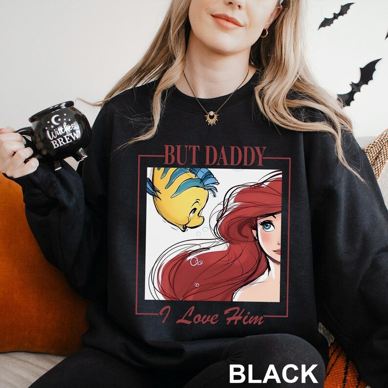 May include: Black crew neck sweatshirt with a graphic of Ariel and Flounder from The Little Mermaid, and the text "BUT DADDY - I Love Him." The word "BLACK" is printed at the bottom. The sweatshirt is a casual style.