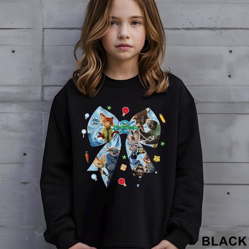 May include: Black sweatshirt featuring a large bow design with characters from the animated film "Zootopia." The bow is decorated with cartoon images of animals and colorful accents. The word "BLACK" is printed at the bottom.