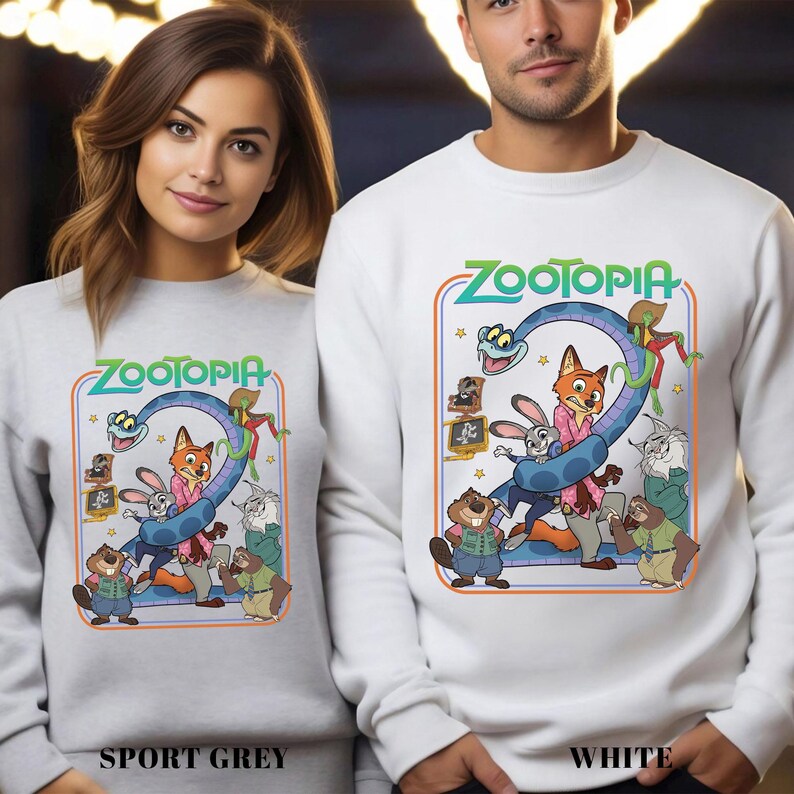 May include: Sport grey and white sweatshirts featuring a colorful graphic from the animated movie Zootopia. The design includes the movie title and various characters like a fox, rabbit, and snake. The sweatshirts are a comfortable, casual style.