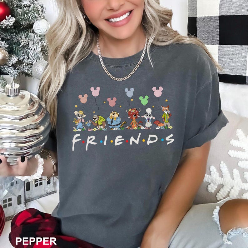 May include: Dark gray t-shirt featuring the word "FRIENDS" in white with colorful dots. Above the word are cartoon characters holding Mickey Mouse balloons. The shirt is a comfortable, casual style.