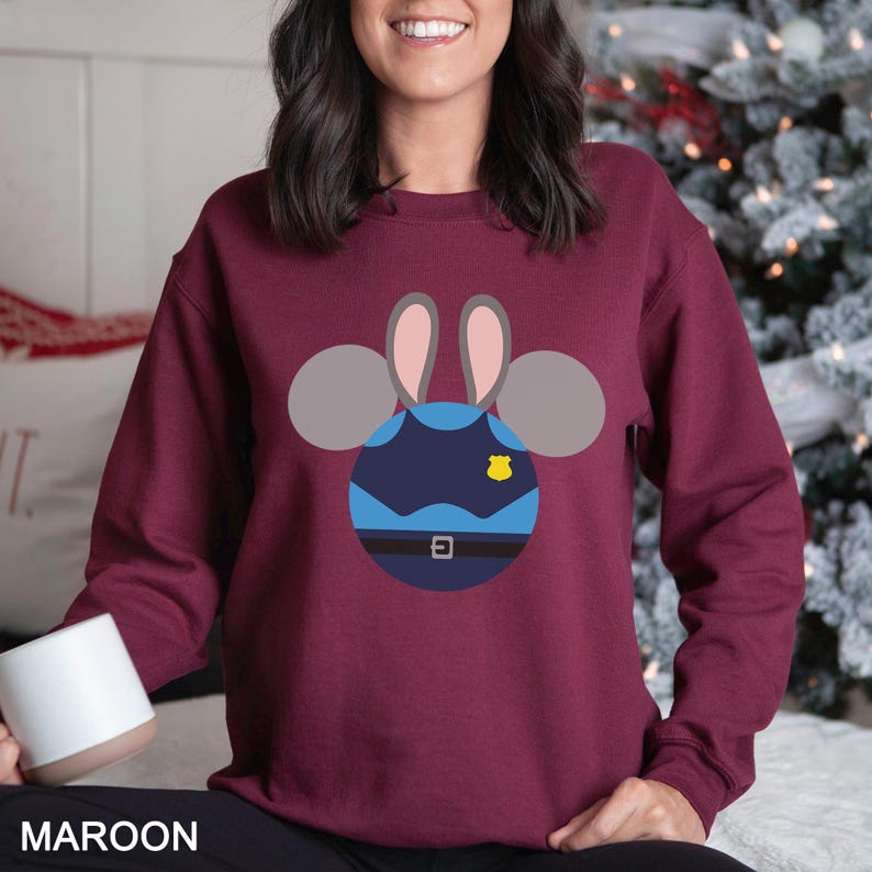 May include: Maroon sweatshirt featuring a cartoon design of a police officer bunny. The design includes a blue uniform, a yellow badge, and gray ears. The word "MAROON" is printed at the bottom of the image.