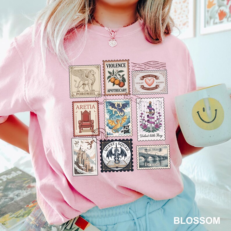 May include: A light pink t-shirt featuring a collection of illustrated postage stamps. The stamps depict various images, including a griffin, a dragon, and a heart. The word "BLOSSOM" is printed at the bottom.