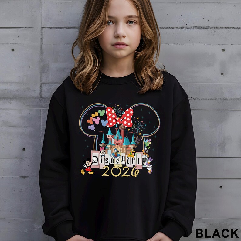Puede incluir: Sudadera negra con un gr&aacute;fico colorido de un castillo, Mickey Mouse, Minnie Mouse y el texto "Disney Trip 2020". El dise&ntilde;o incluye un lazo rojo con lunares blancos y un arco&iacute;ris de cabezas de Mickey Mouse. La sudadera la lleva una persona joven.
