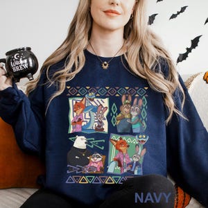 Może przedstawiać: Granatowa bluza z kolorową grafiką postaci z Zootopii w czterech panelach. Projekt zawiera Judy Hopps, Nick Wilde i inne postacie. Słowo "NAVY" jest wydrukowane na dole. Bluza ma okrągły dekolt.