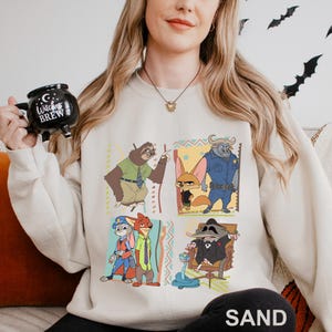 May include: A sand-colored sweatshirt featuring a colorful graphic of characters from a popular animated movie. The design includes four panels with different characters. The word "SAND" is printed at the bottom of the sweatshirt.