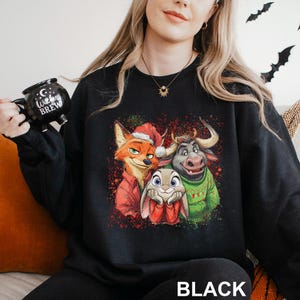 May include: Black sweatshirt featuring a colorful graphic of three cartoon characters: a fox in a Santa hat, a rabbit, and a bull wearing a green sweater. The word "BLACK" is printed at the bottom.